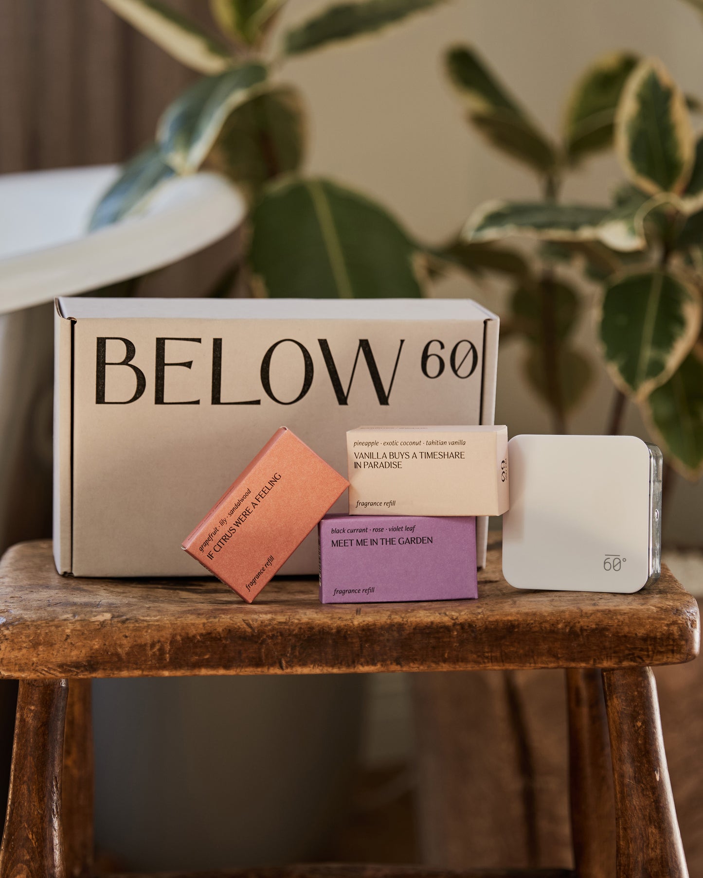 Below 60 Best Sellers Starter Kit with diffuser and three fragrance refills displayed on a wooden stool with lush green plants in the background.