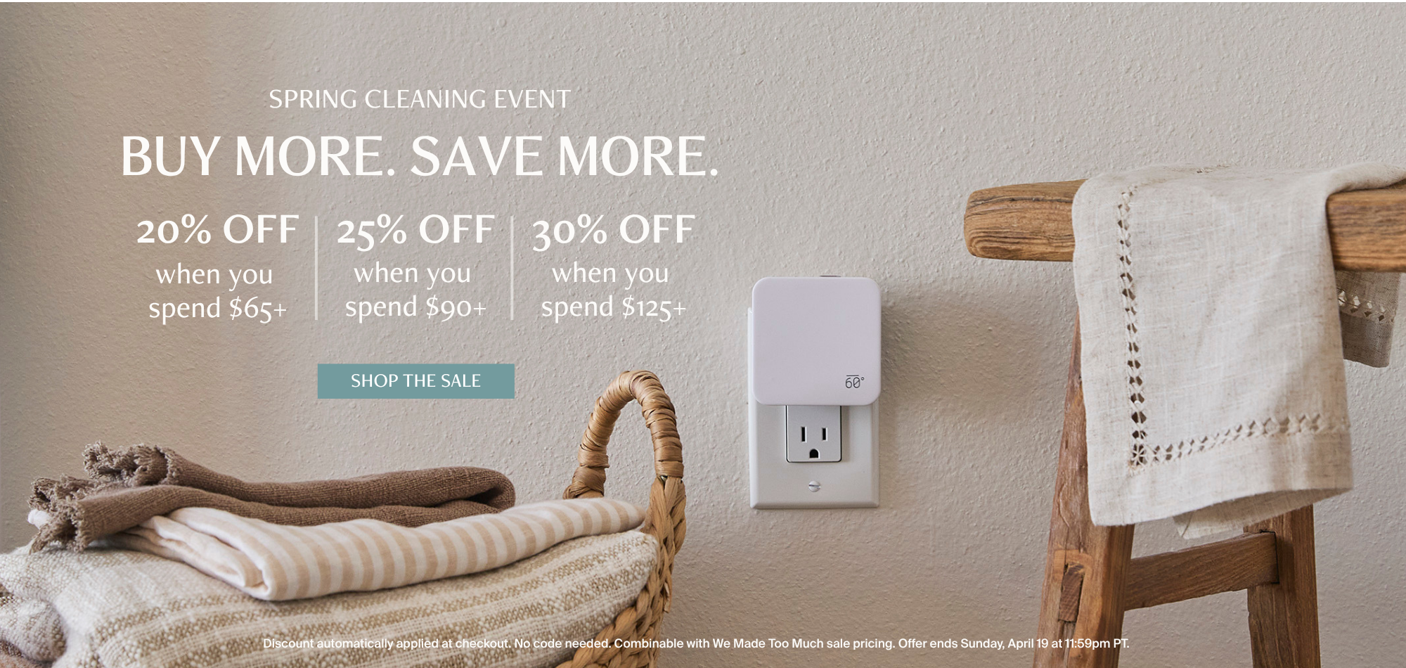 The Below 60 Plug-In Home Fragrance Diffuser plugged into a wall outlet in a warmly lit laundry room, styled with a wicker basket of folded linens and a wooden ladder draped with a linen towel. Text overlay reads: Spring Cleaning Event — Buy More. Save More. — 20% off when you spend $65+, 25% off when you spend $90+, 30% off when you spend $125+.